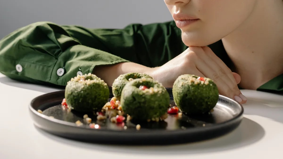 Close-up of spinach pkhali, a Georgian vegan dish, with a woman in green observing.
