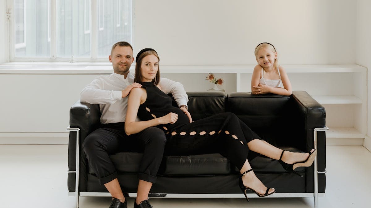 Elegant family photo on a modern sofa, featuring a couple and child dressed in black and white.